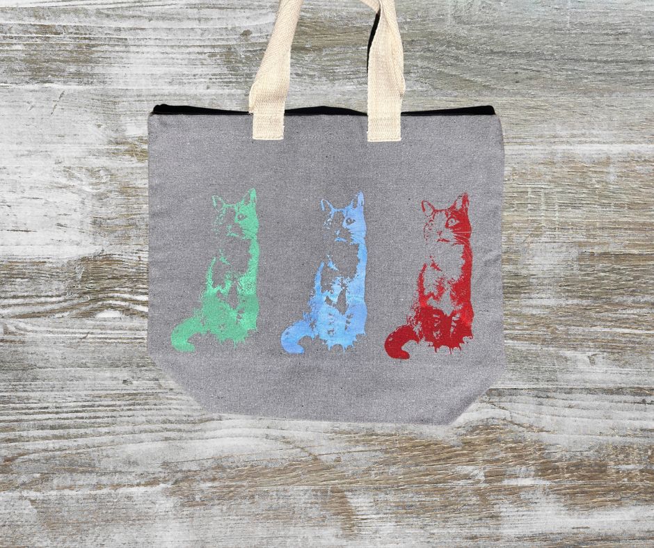 Gray tote bag with colorful cat illustrations on a wooden surface