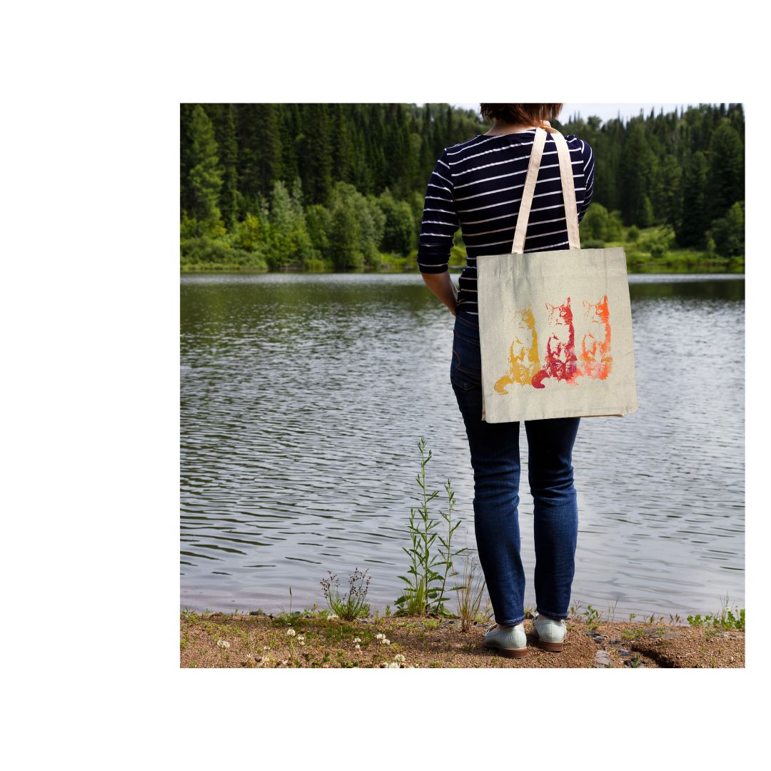 Person holding a tote bag with a colorful cat design by a lake