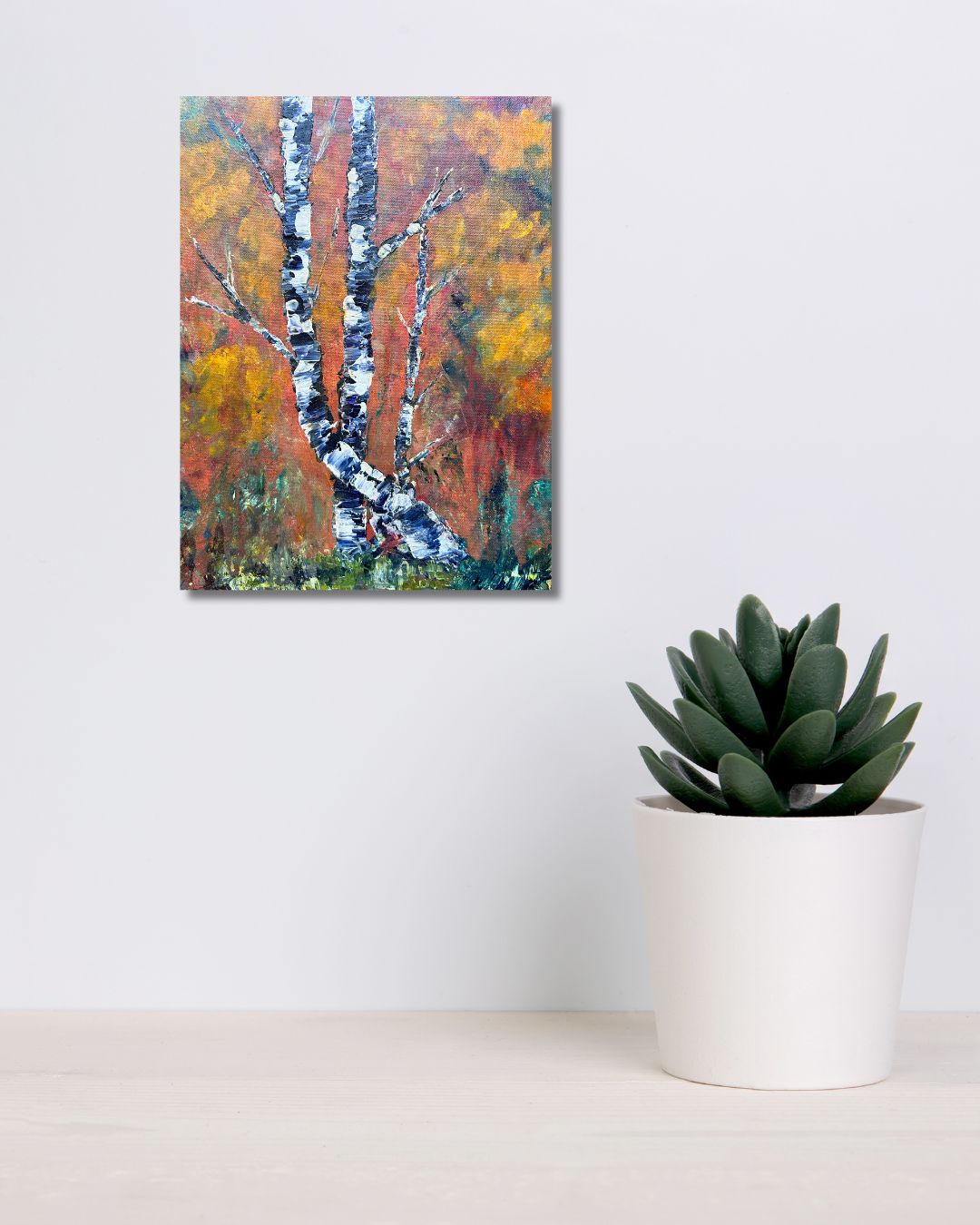 Original acrylic painting by Ottawa artist Mireille Laroche depicting trees with a fall background. Painting on a white wall over a shelf with a green plant.