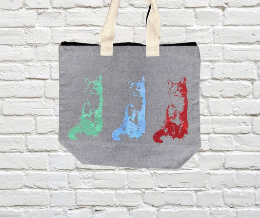 Gray tote bag with colorful cat illustrations on a white brick wall background