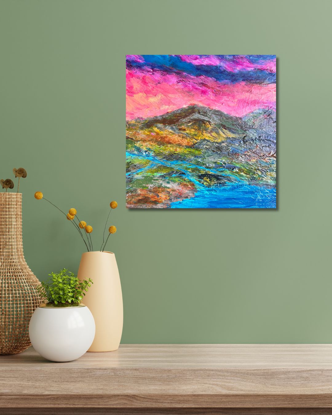 A colorful abstract landscape painting on canvas by Ottawa artist Mireille Laroche,  displayed on a sage green wall above a wooden table with decorative vases and a small plant.