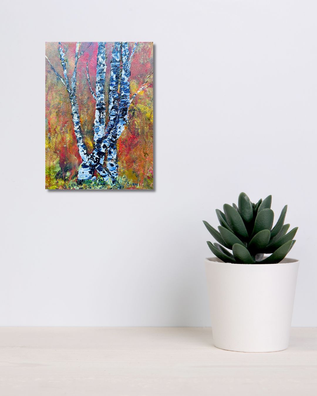 Original acrylic painting by Ottawa artist Mireille Laroche depicting trees with a fall background. Painting on a white wall over a shelf with a green plant. 
