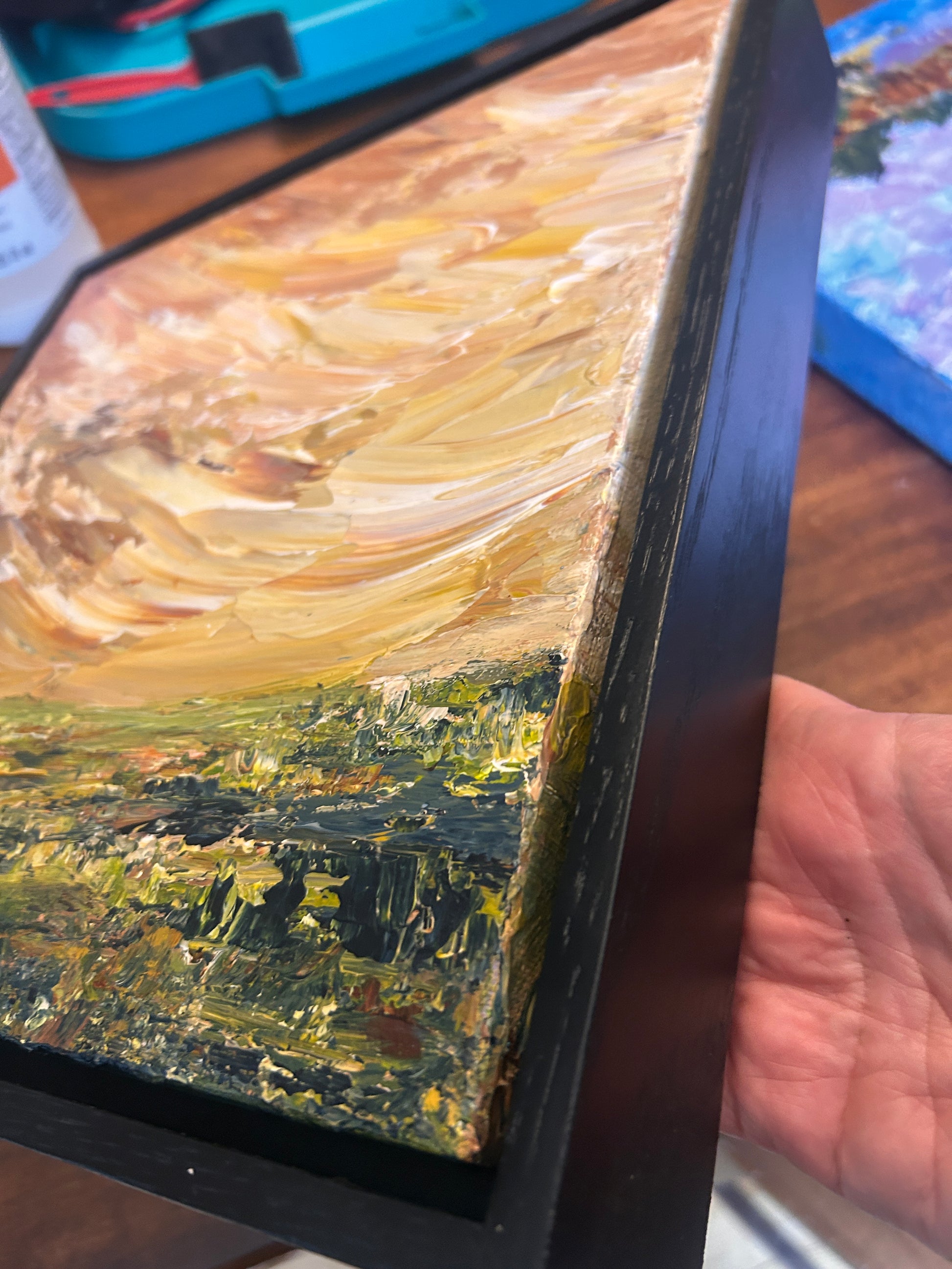 Close-up of a painting with a black frame held by a hand.